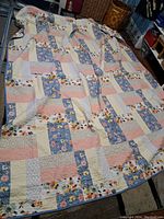 Full view of vintage quilt showing the patchwork front side with multiple fabric patterns including florals and stripes in pastel colors.
