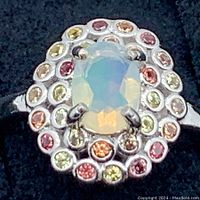 Close-up of the ring showing natural opal center and multi-colour sapphires halo, displaying play of color on opal and vibrant sapphire hues.