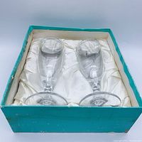 Two Tiffany champagne glasses inside the Tiffany blue box with white silk cushion lining, showing front view and placement of glasses.
