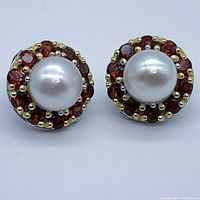Front view of earrings showing pearl center and garnet halo with gold prongs on white gold plated silver base.