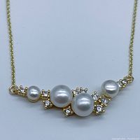 Close-up image of gold-plated pendant necklace showing four white semi-round pearls sized 4-7mm with surrounding clear gemstone accents on pendant chain flat on white background.