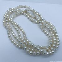 Close-up photo showing the genuine pearl necklace coiled on a flat surface, displaying individual pearls' luster and shape.