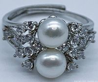 Close-up front view showing two near round white pearls with clear gemstone clusters on both sides and split band design.