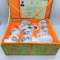 8-piece peach pattern tea set in an orange fabric-lined decorative box with certificate, showing neatly arranged items with white porcelain and hand-painted peaches.