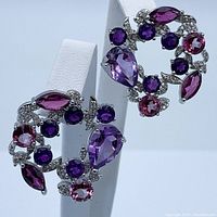 Close-up photo showing front and side view of the pair of circular multi gemstone earrings on white display stand.