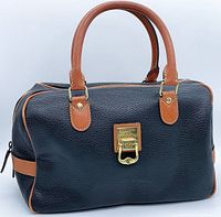 Angle view showing front side of handbag with branded gold-tone clasp, brown leather handles and trim on black leather body.