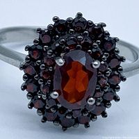 Close-up frontal photo of the ring showing the oval center garnet and surrounding smaller garnet stones with sterling silver band.
