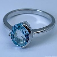 Close-up of oval sky blue topaz gemstone set in sterling silver ring showing color and cut of stone and ring band shape.