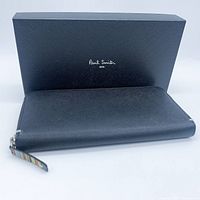 Front side view of the black Paul Smith leather wallet with box in background showing texture and zipper pull detail.