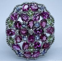 Top view of oval ring showing multiple pear-shaped and round rhodolite garnet stones with interspersed blue sapphires and green stones in a cluster setting on sterling silver.