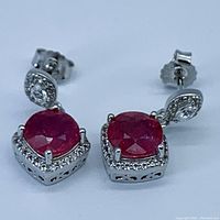Close-up front view of earrings showing round rubies set in square frames with white topaz accents.