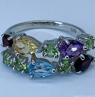 Close-up front view of multi-gemstone sterling silver ring showing pear-shaped citrine, topaz, amethyst, round peridot and garnet stones.