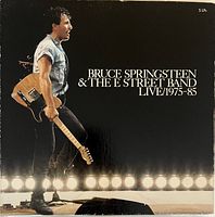 Front cover of the box set showing Bruce Springsteen holding a guitar on stage with lighting in the background. The title on the cover reads Bruce Springsteen & The E Street Band Live/1975-85 and notes it includes 5 LPs.