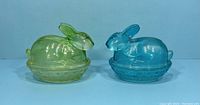 Front view of two glass bunny trinket dishes, yellow-green and blue.