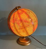 Front view of the illuminated globe showing warm internal lighting highlighting geographic details on the map surface and the brass-colored base and armature.