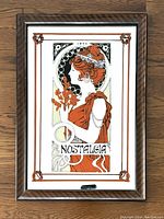 Front view of the rectangular mirror with an Art Nouveau style illustration of a woman in profile holding flowers with ornamental border and a polished wood frame.