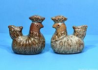Two vintage ceramic chicken salt and pepper shakers shown from the front on a blue background.