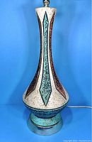 Front view of the chalkware genie table lamp showing the off-white body with teal and brown elongated diamond pattern and metal base.