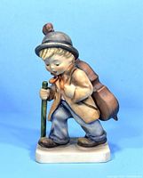 Front view of vintage M.J. Hummel figurine showing boy carrying cello case and holding walking stick.