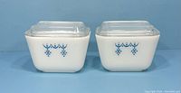 Front view of two identical Pyrex refrigerator dishes with Snowflake Garland pattern and lids.