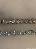 Closeup of two bracelets showing clear round and blue oval stones in silver settings.