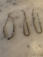 Three sterling silver bracelets laid out on a white surface, showing full length and design, including one broken bracelet.