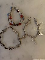 Lot of three sterling silver bracelets including charm bracelet, openwork bracelet and beaded bracelet lying on a marble surface.
