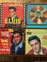 Four Elvis Presley vinyl LP covers shown laid out on wooden floor including 'It Happened at the World's Fair', 'Golden Records Volume 3', 'Girls! Girls! Girls!', and 'King Creole'.