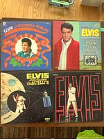Four vintage Elvis Presley LP records on a wooden floor: Elvis Christmas Album, Kisses and Cousins, Aloha from Hawaii via Satellite, and an international Elvis tribute album.