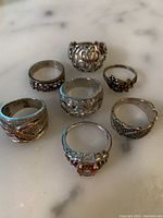 Seven sterling silver rings on a marble surface showing variety of designs and stones