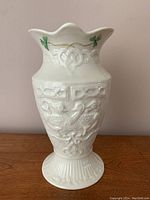 Front view of the white porcelain Belleek vase showing raised relief swan design and green shamrock decoration near rim.