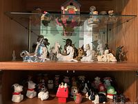 Glass shelf displaying ceramic horse and unicorn figurines, various colors including white and brown, along with smaller decorative pieces.