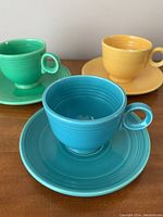 Three Fiestaware cups and saucers in green, yellow, and blue, showing full sets.