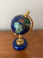 Image showing side view of the miniature stone globe on a brass stand with blue base on a wooden surface.