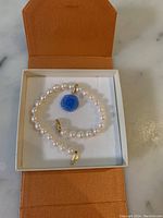 Pearl bracelet with blue rose-shaped pendant displayed in an orange box.