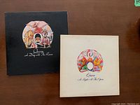 Two Queen vinyl LP album covers showing 'A Day at the Races' with a black cover and 'A Night at the Opera' with a white cover featuring the Queen emblem.