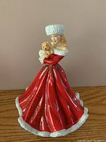 Full view of Royal Doulton Christmas Surprise figurine showing woman in red dress holding a puppy.