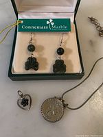Green Connemara marble shamrock earrings on hooks in green box with tag. Sterling silver necklace chain with three charms: Good Luck coin with clover, heart with black rose, wishbone charm pendant.