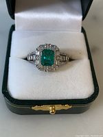 Front view of ring in presentation box showing emerald green center stone and clear stone halo