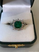 Top-down view of ring in presentation box showing green center stone and halo of clear stones