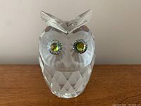 Front view of clear Swarovski crystal owl with green eyes, faceted body, and frosted face details.