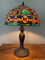 Front angle of Tiffany style lamp showing colorful stained glass shade lit and detailed metal base.