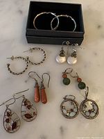 Full set of seven pairs of sterling silver earrings arranged on table with black box containing one pair.