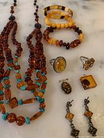 Overview of entire lot showing amber necklace with turquoise beads, bracelets, rings, earrings, brooch, and pendant on marble surface