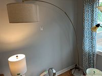 Full view showing the lamp's arched design and beige drum shade extending from the brass arm.