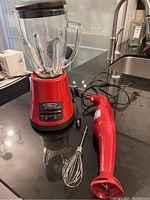 Oster countertop blender with glass jar and PC red hand blender with whisk on black countertop