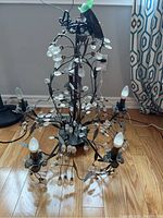 Full view of the metal chandelier featuring five lights and numerous acrylic leaf decorations, photographed on a wooden floor.