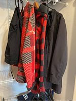 Four items hanging on rack: two plaid coats, one black jacket, and one pair of black pants on hanger.