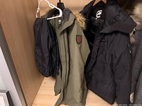Two coats and black snow pants hanging on hangers in a closet shelf