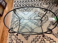 Top-down view of the oval glass top showing the wrought iron supporting frame beneath.